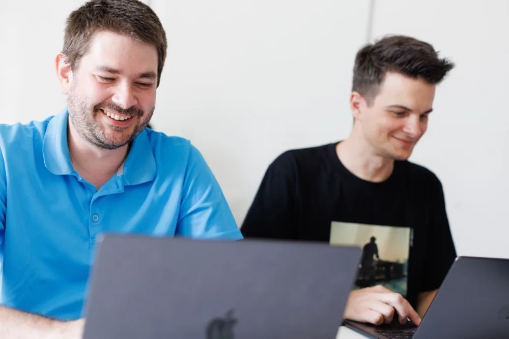 Two team members smiling while working on their laptops